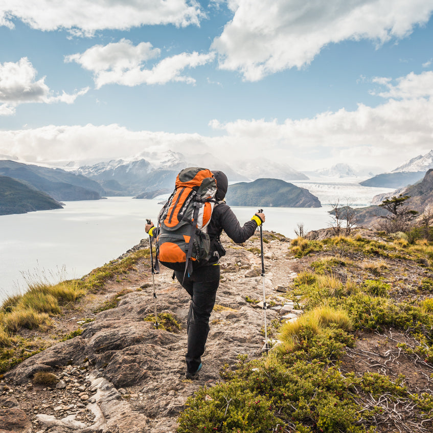 Person hiking outdoors during daytime near water and mountains