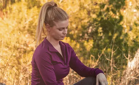 woman sitting down wearing burgundy long sleeve merino wool zip up and grey leggings