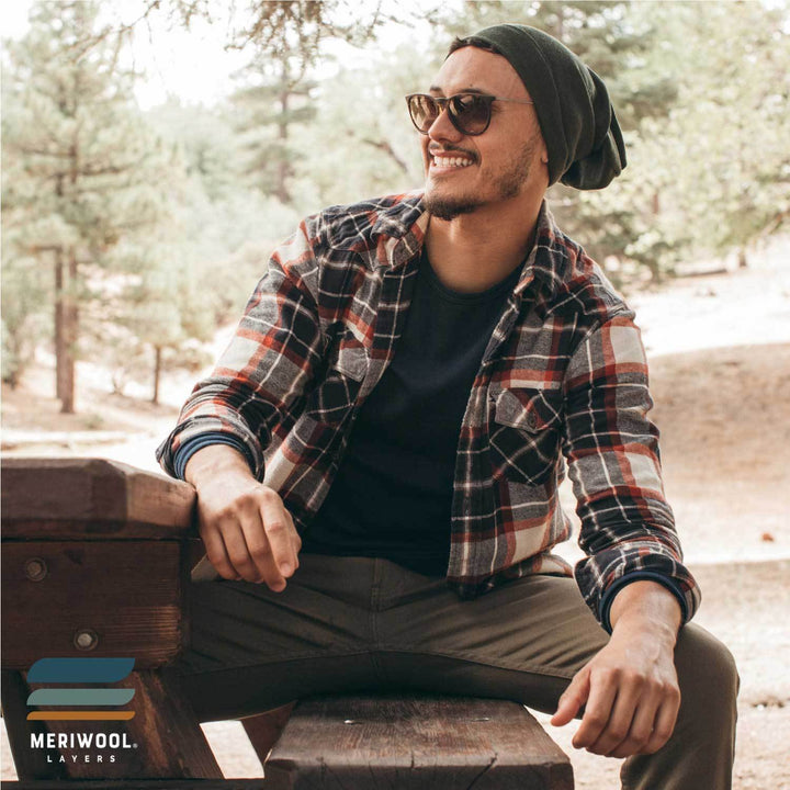 man sitting on a camping bench wearing an army green merino wool 250 cuffed beanie